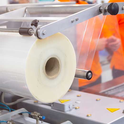 Close-up of a large roll of clear plastic film being fed into an industrial packaging machine.