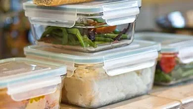 Clear, locking-lid glass containers, filled with prepped meals, stacked on a kitchen counter.