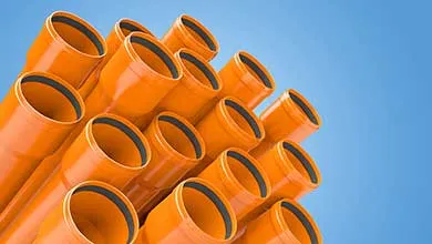 Low-angle shot: Bright orange PVC pipes with black seals against a clear blue sky.