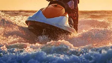 Jet skier on choppy water at sunset, kicking up spray.
