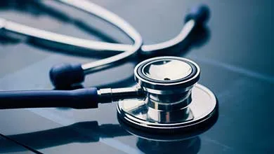Close-up of a stethoscope's metal chest piece on a dark, reflective surface.