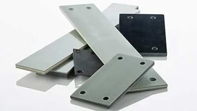 A pile of overlapping rectangular composite plates in shades of gray and black, some with mounting holes at the corners, on a white surface.