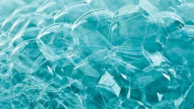 Close-up of clustered translucent blue soap bubbles of varying sizes, with glossy surfaces reflecting light.