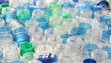 Large collection of clear, blue, and green plastic bottle necks arranged closely together, representing packaging materials.